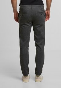 Pantalons de jogging gris, ajustés, avec une texture douce, une taille élastique, deux poches arrière et une coupe fuselée. Portés avec des chaussures de couleur claire.