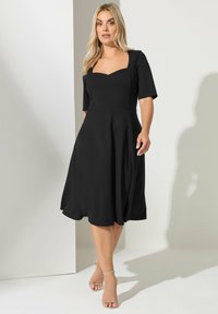 Vestido negro con escote cuadrado, mangas cortas y falda acampanada. Hecho de una tela suave, presenta un corsé ajustado y un dobladillo suelto.