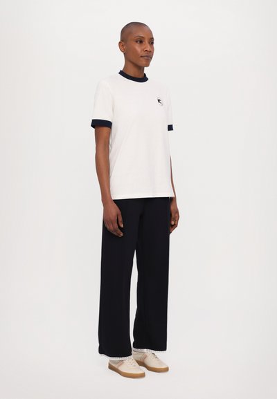 White short-sleeve t-shirt with a navy collar and cuffs, paired with wide-leg navy pants and cream sneakers with brown soles.