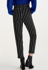 Pantalon rayé noir et blanc à taille haute et jambe fuselée, avec un ourlet retroussé. Assorti à des bottines noires à talons.