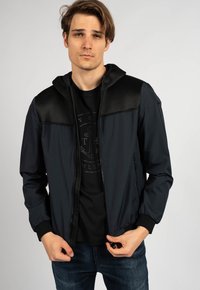 Giacca bomber da uomo con corpo di un blu navy scuro, spalle in tessuto a rete nero, chiusura con zip, tasche laterali e polsini a coste.