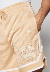 Beige Netz-Sport Shorts mit weißen Seitenstreifen, versehen mit einem gestickten "World Series 2001"-Logo am linken Bein.