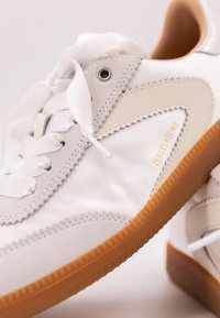 Vita sneakers med en slät tygövre, mockadetaljer, lager-på-lager-design och en sula av gummigummi. Har en dekorativ snörning.