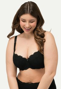 Reggiseno in pizzo nero con ferretto, caratterizzato da bordi scallop, spalline regolabili e una chiusura centrale. Motivo floreale dettagliato su tutta la stoffa.