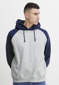 Grijze en marineblauwe hoodie met een raglanontwerp, voorzien van een voorzak en een kleine tekstdetail "A.R.C." op de borst. Zacht materiaal.