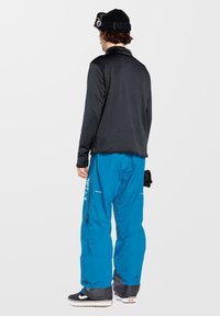 Zwarte lange mouw top gecombineerd met felblauwe sneeuwbroek. De broek heeft ritsen en merkopdruk aan de zijkant. Getextureerde stof op de top.