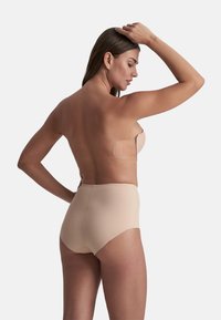 Nude strapless bh met zelfklevende vleugels, gecombineerd met high-waisted, naadloze slipjes. Soepele textuur, minimalistisch ontwerp en huidskleur.