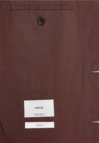 Tissu marron avec une grande poche boutonnée et deux étiquettes blanches cousues indiquant « MNG » et « SLIM FIT » sur la partie inférieure du tissu.