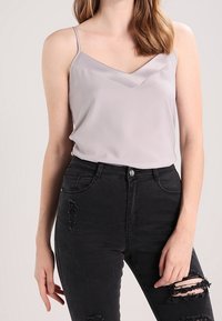 Top in satin grigio chiaro con scollatura a V e spalline sottili, abbinato a jeans neri a vita alta strappati.