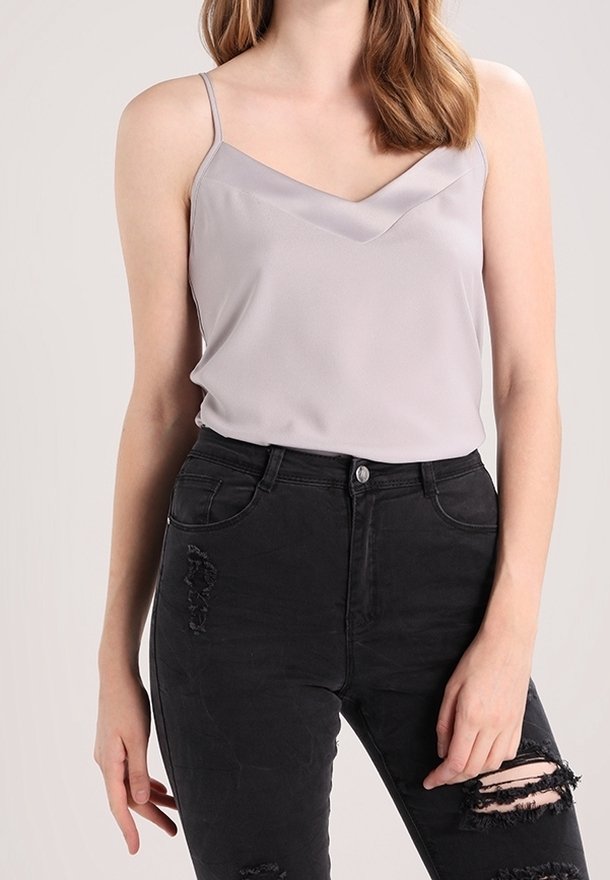 Top in satin grigio chiaro con scollatura a V e spalline sottili, abbinato a jeans neri a vita alta strappati.