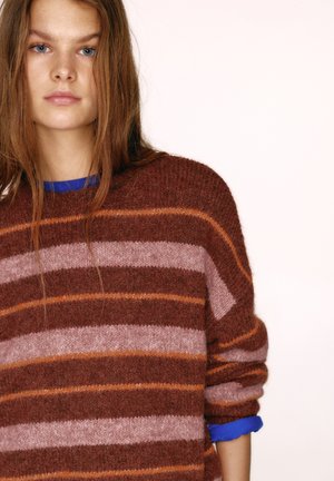 Kötött pulóver barna, rózsaszín és narancssárga csíkokkal. Puha textúra, leejtett vállak és kék részlet a belső galléron.