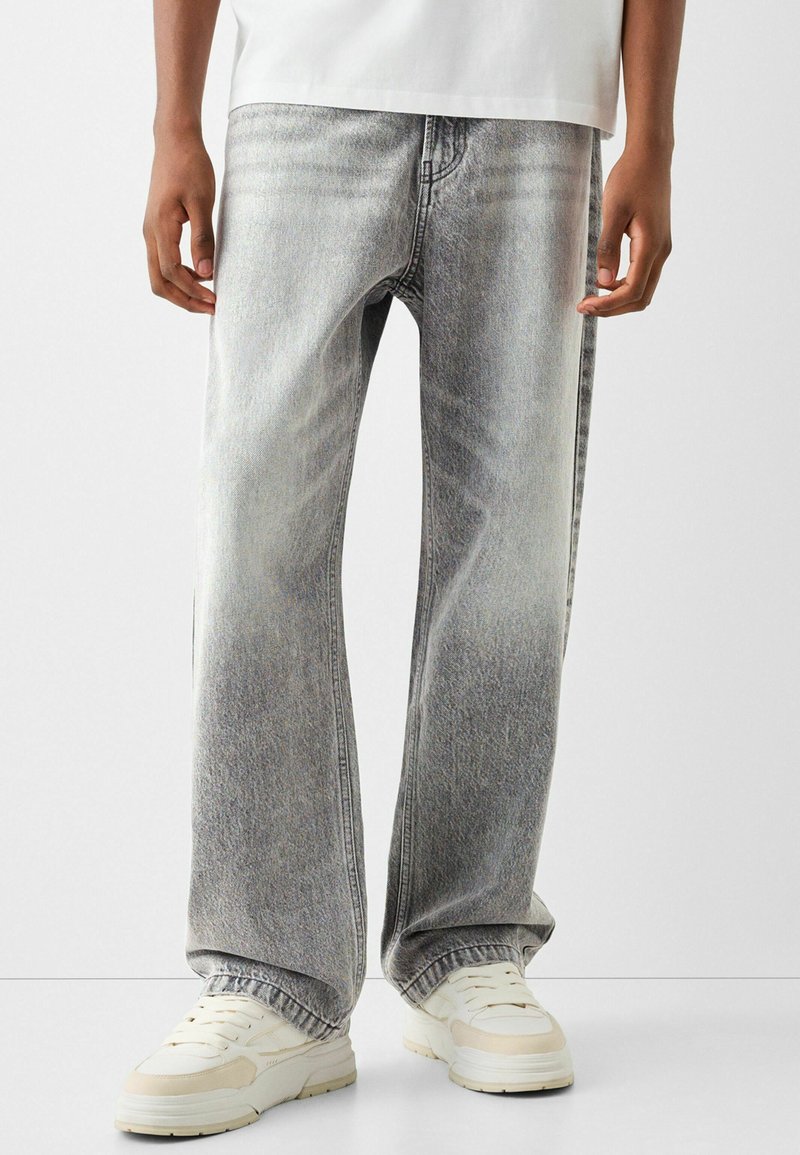 Een paar lichtgrijze, loose-fit denim jeans met een vervaagde afwerking. Voorzien van gestikte zakken en een rechte pijpdesign. Gedragen met witte sneakers.