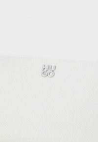 Balta tekstūruota odinė piniginė su sidabriniu "HUGO" logotipu. Medžiaga turi akmenuotą apdailą, suteikiančią subtilų taktilinį akcentą.