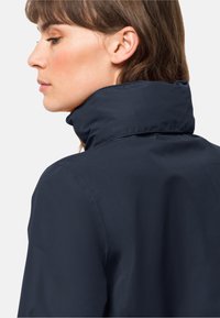 Veste col bleu marine avec un col montant, texture lisse et design élégant visible de dos, mettant en valeur la forme et le matériau du col.