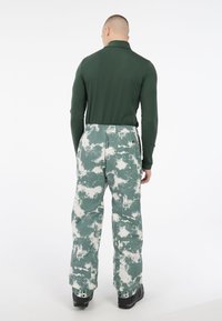 Groene lange mouwen top gecombineerd met een patroonloze, lichtgroene en witte, wijduitlopende broek met een elastische tailleband en zijzakken.