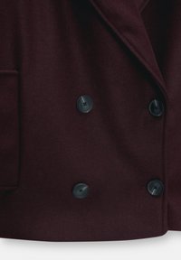 Manteau en laine bordeaux foncé à double boutonnage avec quatre grands boutons noirs visibles près de la fermeture avant.