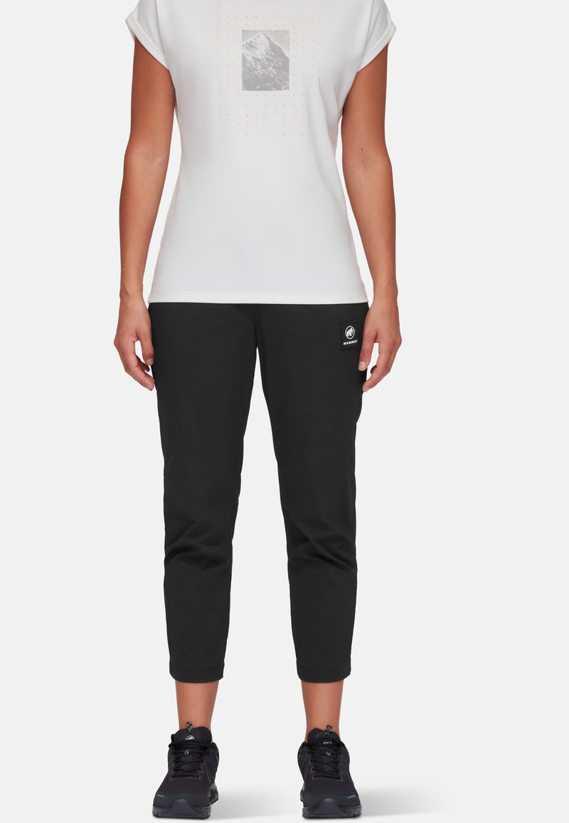 Biała bluzka z krótkim rękawem z grafiką gór, czarne spodnie 3/4 z logiem. Czarne obuwie dopełnia stylizację.