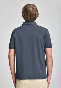 Polo shirt gris oscuro con mangas cortas, un cuello estructurado y una textura sutil. Diseño casual con un dobladillo recto y sin patrones visibles.