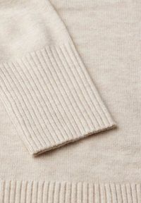 Panno di maglione beige lavorato a maglia con polsini a costine. La trama è morbida e liscia, con un leggero e sottile motivo che attraversa l'intero tessuto.