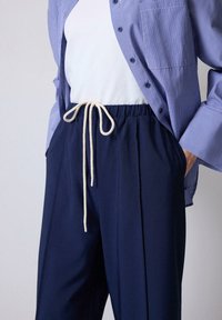 Pantalones azul marino con una cintura elástica, que presentan una textura suave y bolsillos laterales, combinados con una camisa de botones a rayas.