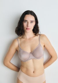 Light beige bra with a smooth texture, adjustable straps, and a small bow detail at the center. Paired with a matching beige brief.