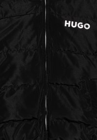 Crna zimska jakna s patentnim zatvaračem sprijeda i horizontalnim šavovima. "HUGO" logo u bijeloj boji na lijevoj strani prsnog koša. Glatka, sjajna tekstura.