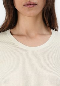 Heledbeez ribade kudumispoolika ümmarguse kaelusega, millel on pehme tekstuur ja kerge läige. Kangas näeb välja kergelt läbipaistev.