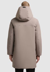 Bézs színű bélelt parka nagy kapucnival, hosszú ujjakkal és egyenes szabással, minimális díszítéssel és puha, texturált felülettel.