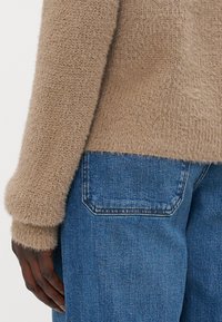 Maglione beige peloso con una texture a coste e una vestibilità rilassata, abbinato a jeans di denim blu con un classico design della tasca posteriore.