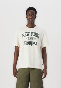 Cremefarvet bomulds T-shirt med teksten "NEW YORK a City in BLOOM" i grøn, med et afslappet fit og korte ærmer.