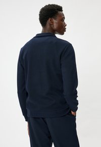 Chaqueta de punto azul marino con un tejido texturizado, mangas largas y cuello; presenta un corte relajado y un acabado suave en el dobladillo.