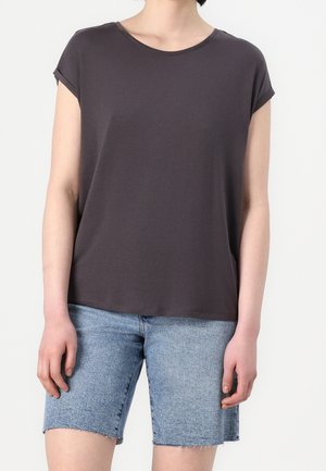 Woman wearing a dark gray short-sleeve loose T-shirt and light blue denim knee-length frayed shorts against a plain background.