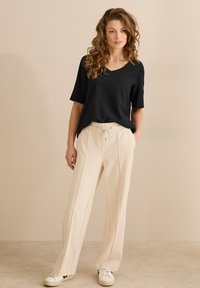 Sort tekstureret T-shirt med korte ærmer parret med beige plisserede bukser og hvide sneakers, med elastisk talje og snøre.
