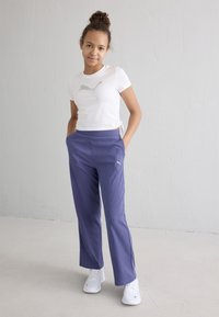 Λευκό κοντομάνικο μπλουζάκι με ανακλαστικό λογότυπο, συνδυασμένο με άνετους, ριμπέ παντελόνες σε μοβ χρώμα και λευκά αθλητικά παπούτσια.