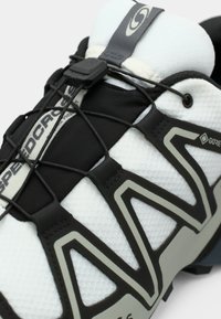 Sapatilha de trail running em preto e branco com parte superior em malha texturizada, atacadores elásticos e sola curva. Apresenta a marca 'SPEEDCROSS' em monocromático.