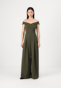Tuta senza spalline di color verde oliva con corpetto aderente, gambe ampie plissettate e scollatura a V. Tessuto morbido e design strutturato.