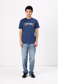 Granatowa bawełniana koszulka z kwiatową grafiką i napisem, zestawiona z jasnoniebieskimi dżinsami i czarnymi sneakersami. Proste krótkie rękawy, okrągły dekolt.