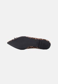 Γυναικείο παπούτσι με λεοπάρ σχέδιο, ακουμπισμένο στο πλάι, που δείχνει την μαύρη, μυτερή σόλα του σε λευκό φόντο.