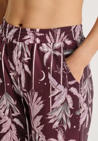 Bordeaux broeken met een tropisch bladerenpatroon in roze en groene tinten. Voorzien van een elastische tailleband en een zijzak. Glad textuur.