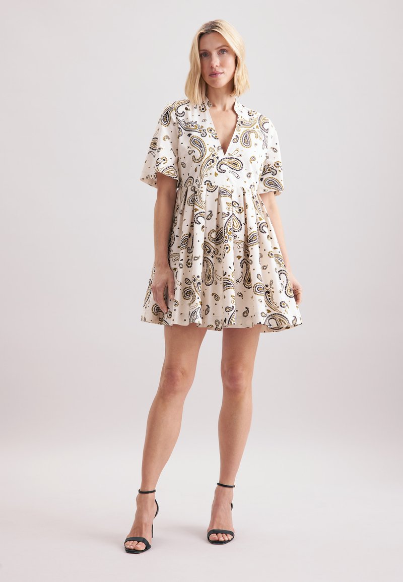 Robe blanche à imprimé paisley avec des manches courtes, un décolleté plongeant et une jupe évasée ; associée à des talons noirs à bride de cheville.