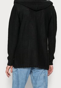 Svart stickad hoodie med ett texturerat mönster, långa ärmar och ribbade muddar, som har en luftig passform och en huva bak.