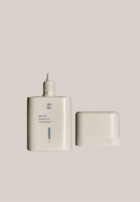 Natural Radiance Foundation w matowej, off-white butelce z zakrętką. Tekst: "95+100" oraz "KORRES". Gładki, minimalistyczny design.