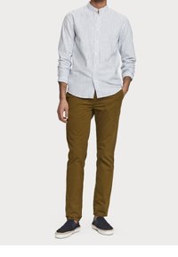 Chemise boutonnée rayée bleu clair avec col montant, associée à un chino vert olive et des chaussures slip-on navy, avec un design texturé.