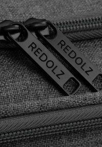 Grijze stoffen zak met twee zwarte ritssluitingen gelabeld "REDOLZ." De textuur is geweven met een gladde ritssluiting.