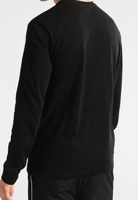 Black long-sleeve T-shirt made of soft fabric, featuring a round neckline and minimal design with a smooth texture and no visible logos.