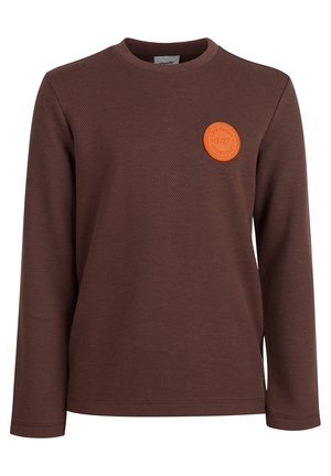 Brązowa koszulka z długim rękawem i okrągłym dekoltem z małą okrągłą pomarańczową naszywką na lewej piersi z napisem "Limited Edition 07."