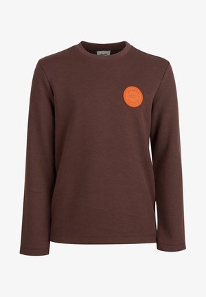 Brązowa koszulka z długim rękawem i okrągłym dekoltem z małą okrągłą pomarańczową naszywką na lewej piersi z napisem "Limited Edition 07."