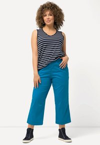 Marinblå och vit randig ärmlös linne kombinerat med klara turkosa vida byxor och marinblå högskor. Slät tyg och avslappnad passform.