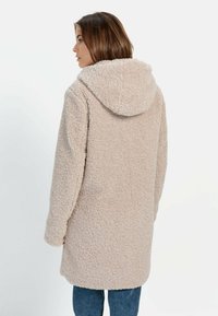 Beige, flauschiger Kunstpelzmantel mit Kapuze, lässiger Schnitt und langen Ärmeln, der bis zur Mitte des Oberschenkels reicht. Strukturierter, weicher Stoff.