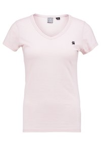 Světle růžové dámské tričko s krátkým rukávem a výstřihem do V, se malým černým logem na levé straně hrudníku a viditelnými štítky na límci.